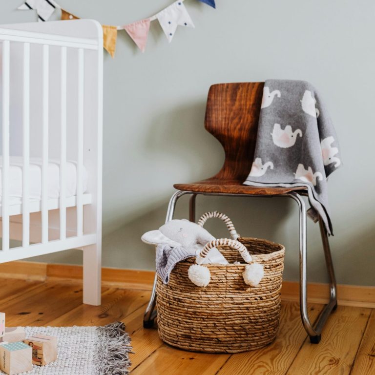 A wooden chair with a grey blanket and a woven basket in a bright nursery setting.