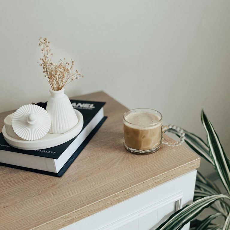 A coffee cup beside a decorative vase and a book on a wooden surface.