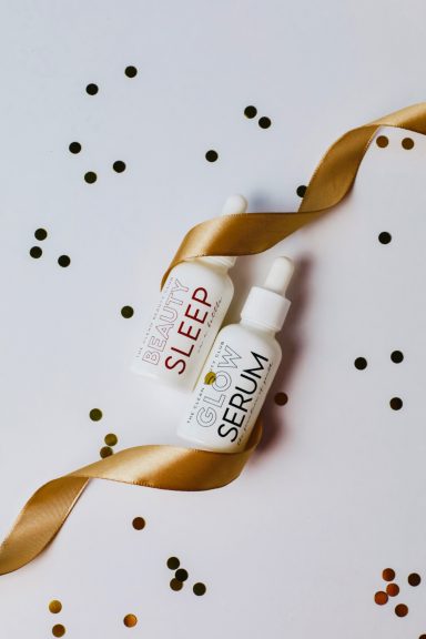 Two skincare serum bottles labelled "SLEEP" and "SERUM" beside a gold ribbon and confetti.
