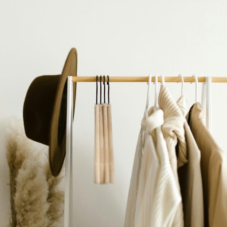 A hat and neutral-toned clothing hang on a wooden rail with a decorative touch.