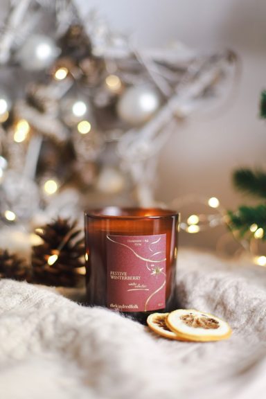 A scented candle with dried orange slices and pine cones, set against a festive backdrop.