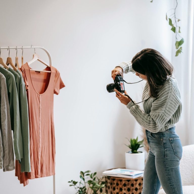 A woman photographs clothing on a rack in a bright, minimalist room.