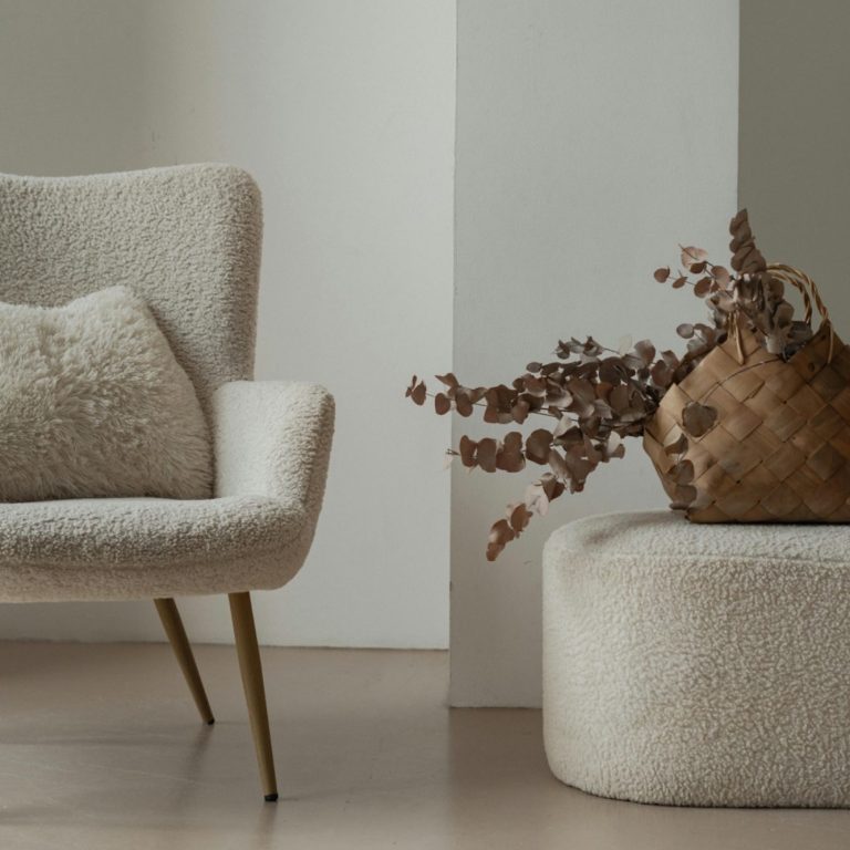 A soft-textured armchair and ottoman with a decorative dried flower arrangement.