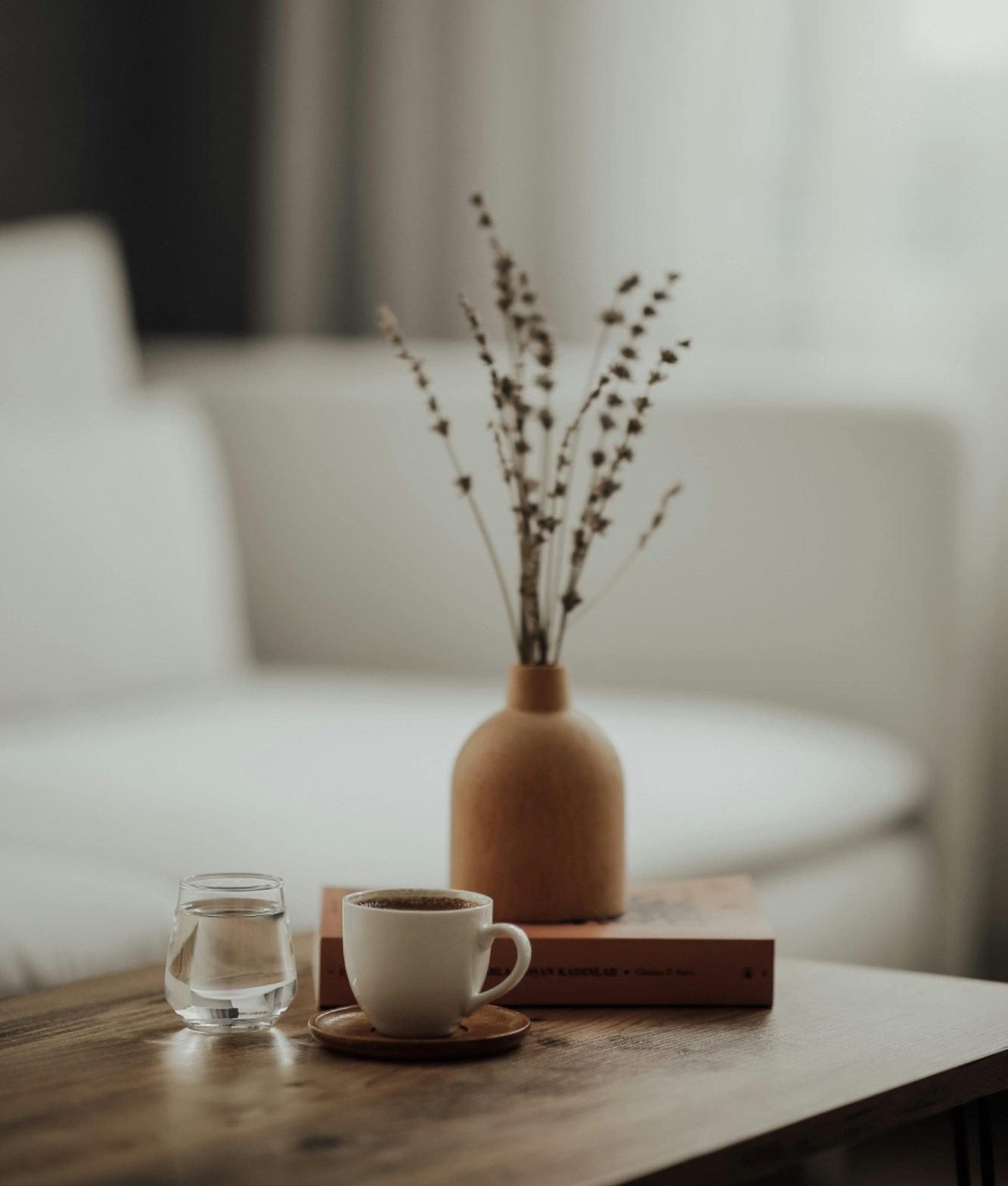 A small vase with dried branches next to a coffee cup on a wooden table.