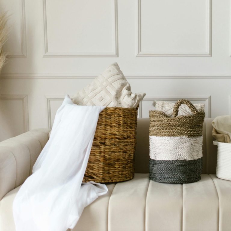 Two woven baskets with cushions on a light sofa against a textured wall.