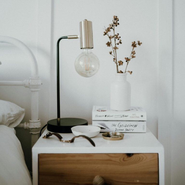 Table lamp, dried flowers in a vase, and stacked books on a bedside table.