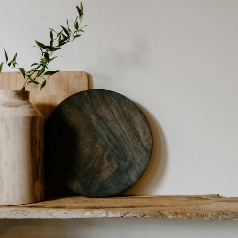 A dark wooden plate, a vase, and cutting boards on a rustic shelf with greenery.