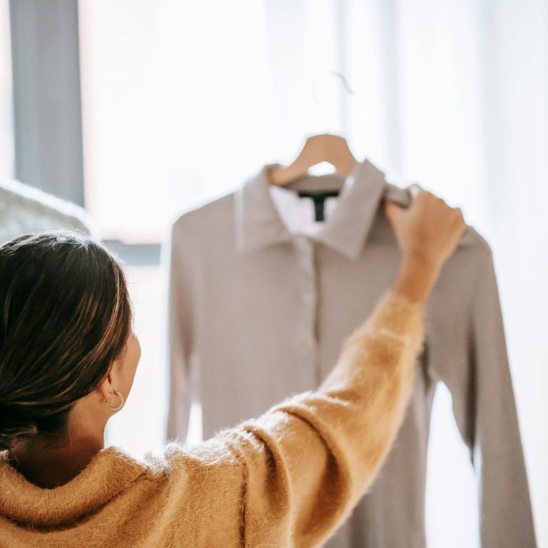 A person reaching for a grey shirt hanging on a rack.