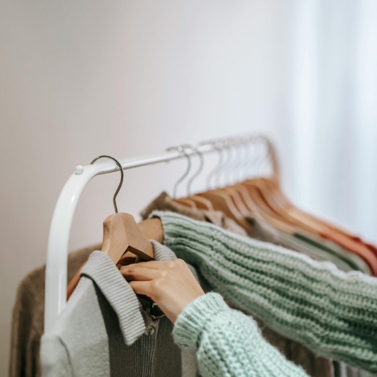 A person selecting a garment from a rack of hanging clothes.